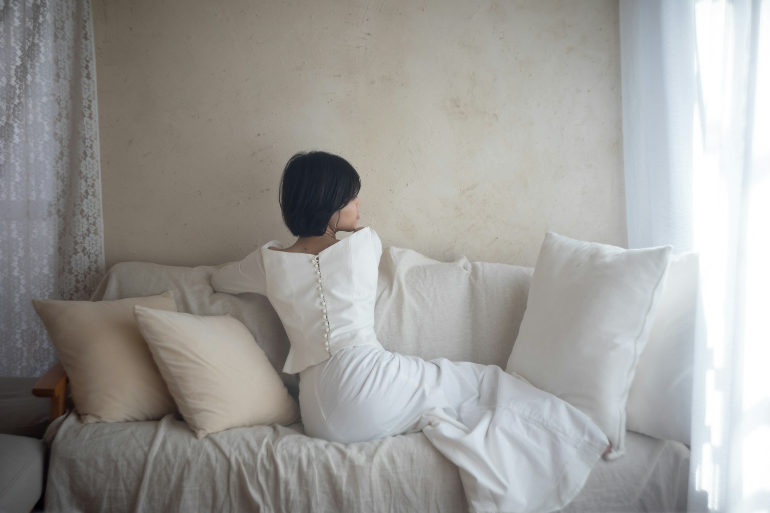 白いドレスを着た女性がソファに寄りかかっているシーン 窓からの自然光が柔らかく差し込む