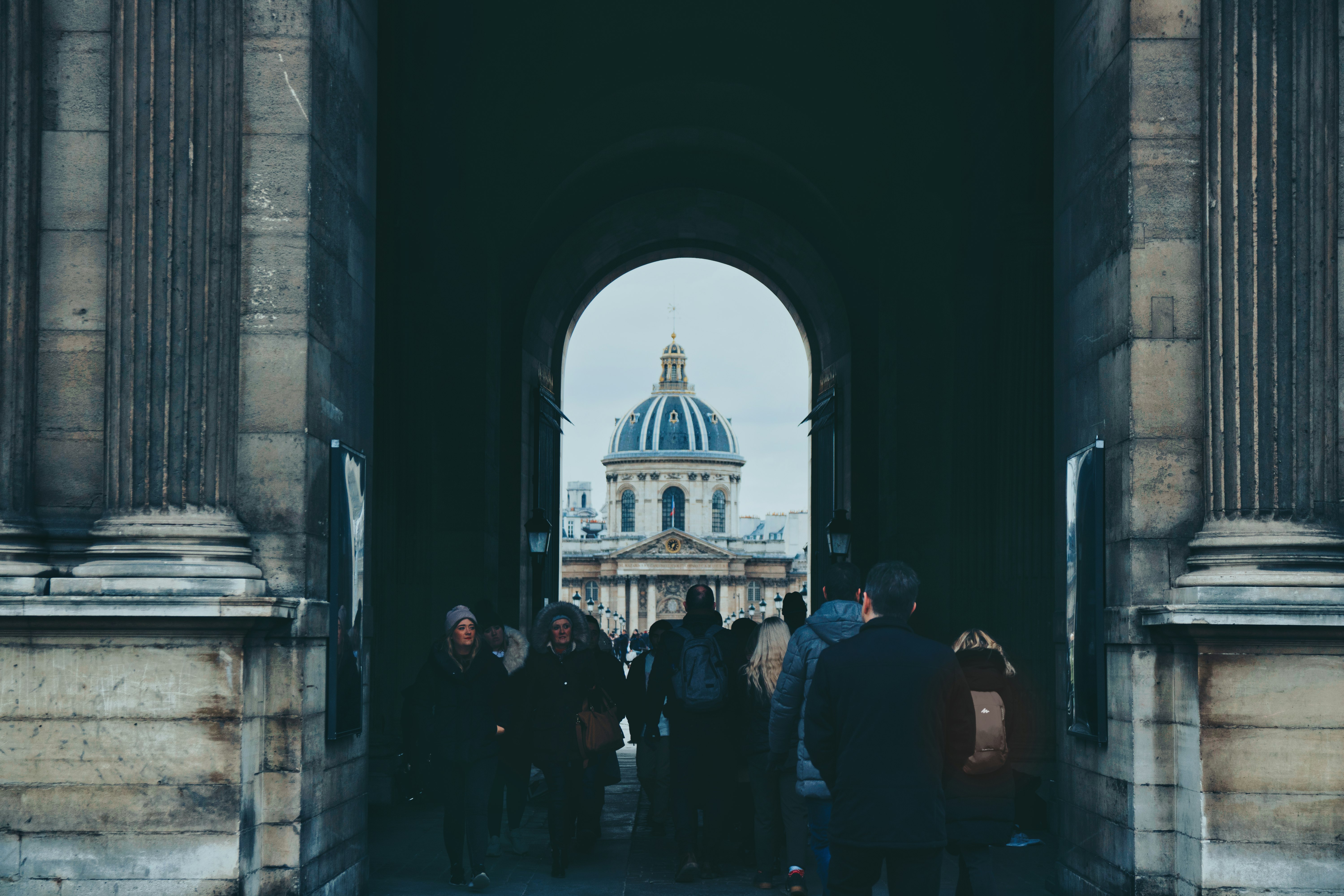 people walking through a stone archway toward a domed building
