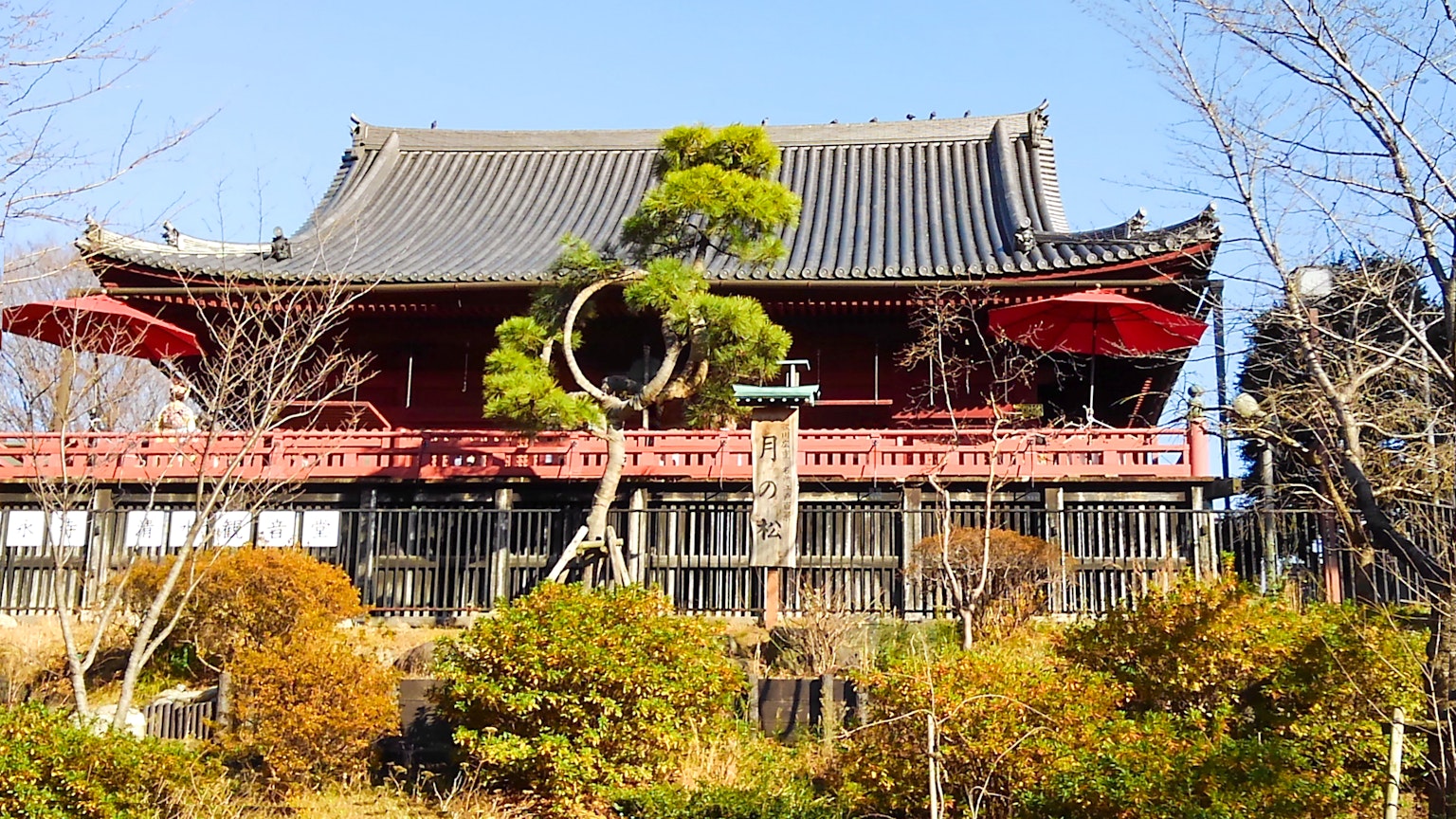 传统日本建筑，红色栏杆和瓦屋顶，周围有绿色树木和花园