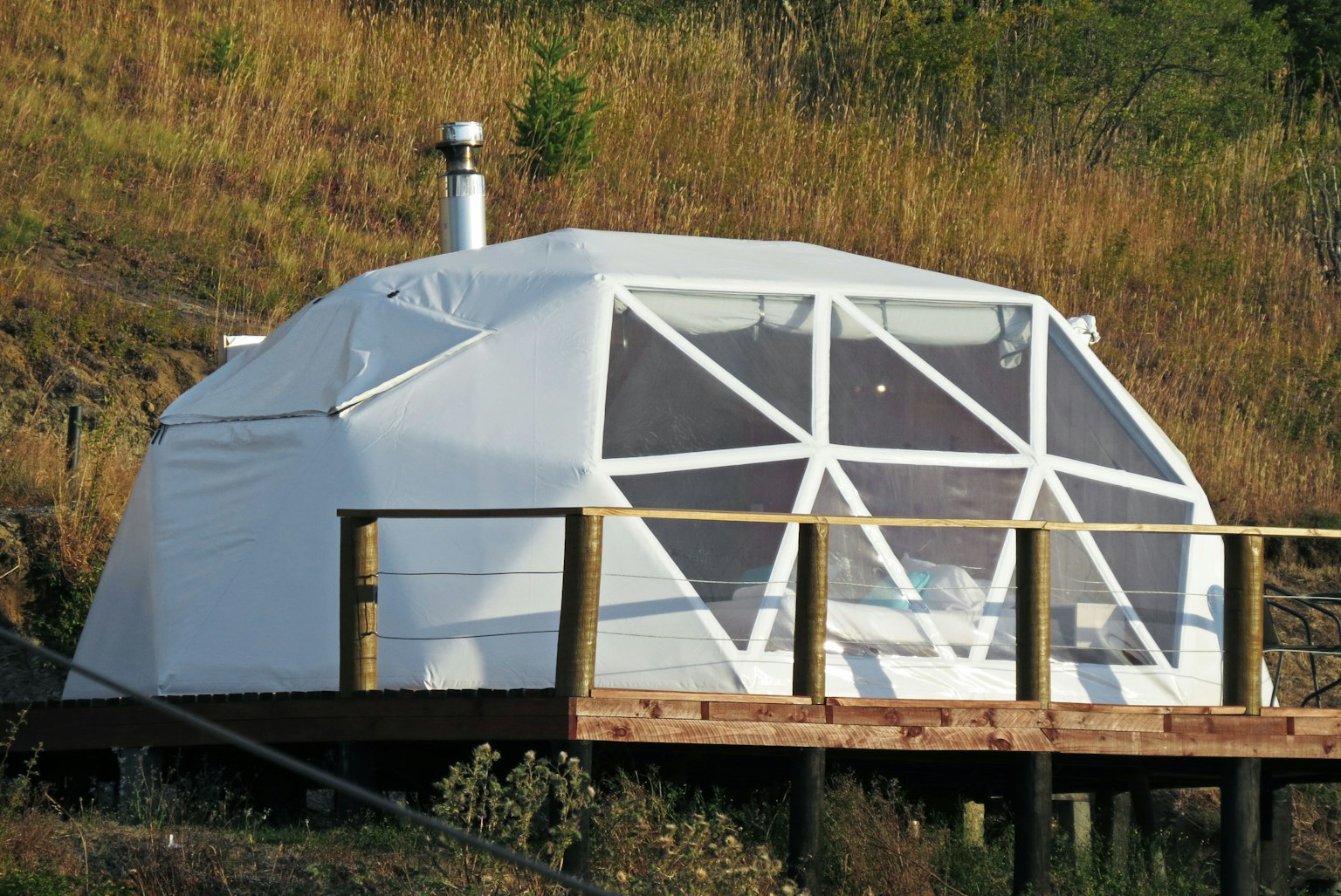 White dome-shaped tent on a wooden deck surrounded by grassy land