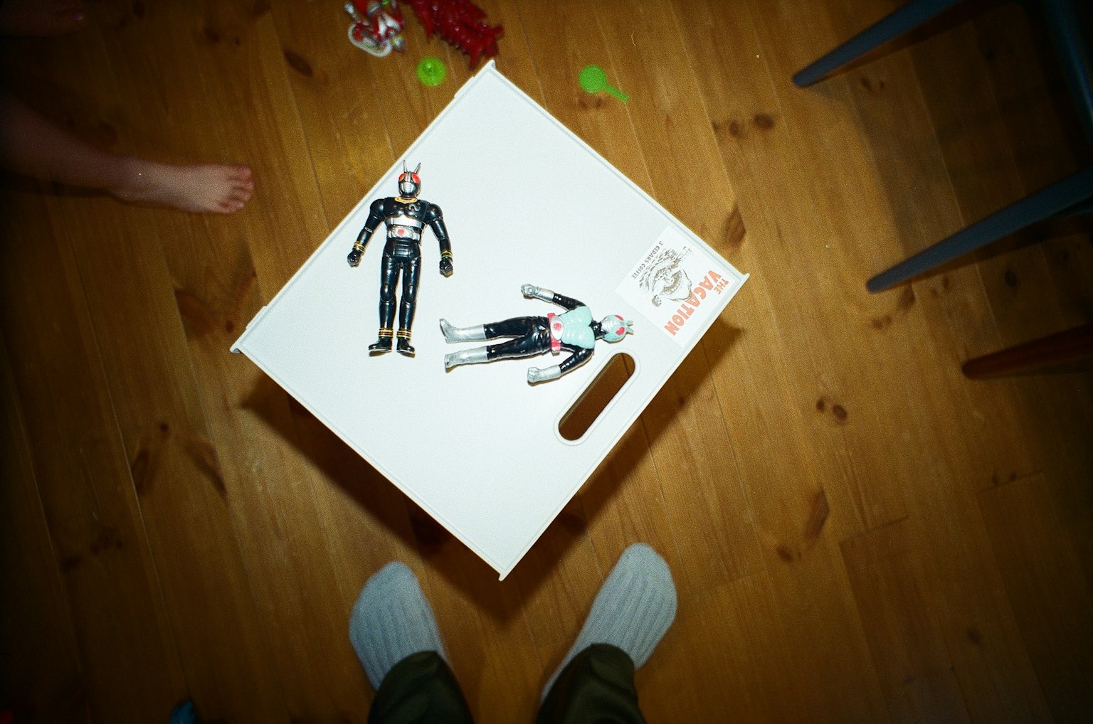 Top view of a white box with toy figures on it showing wooden floor and feet