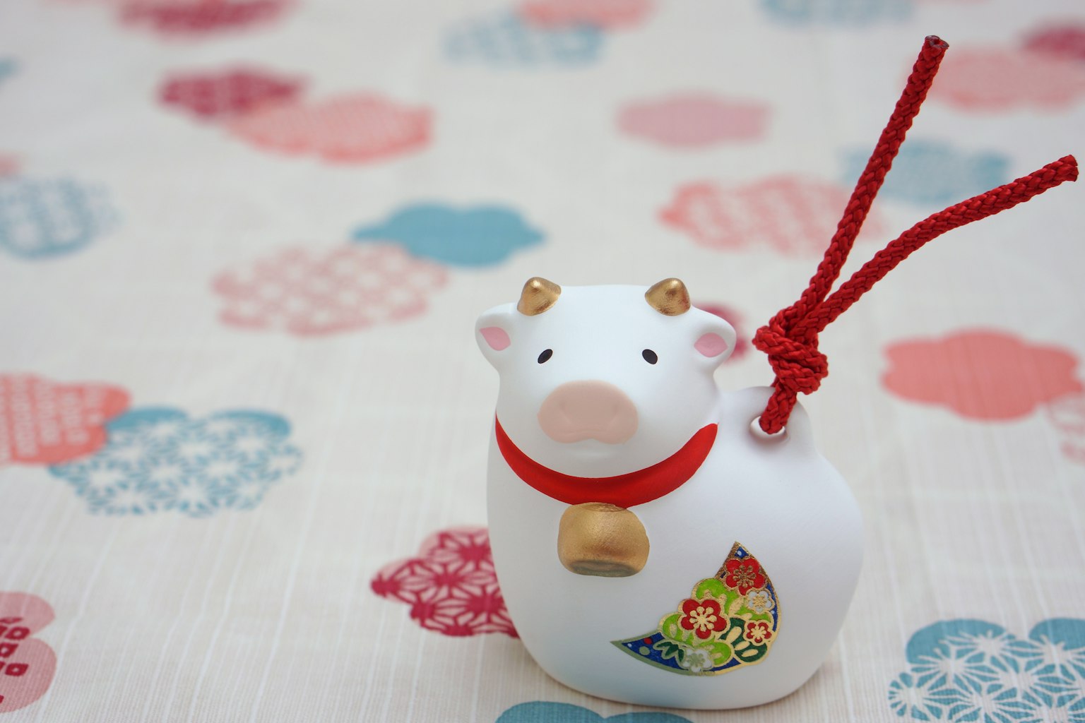 White cow figurine with a red string and bell colorful floral pattern background