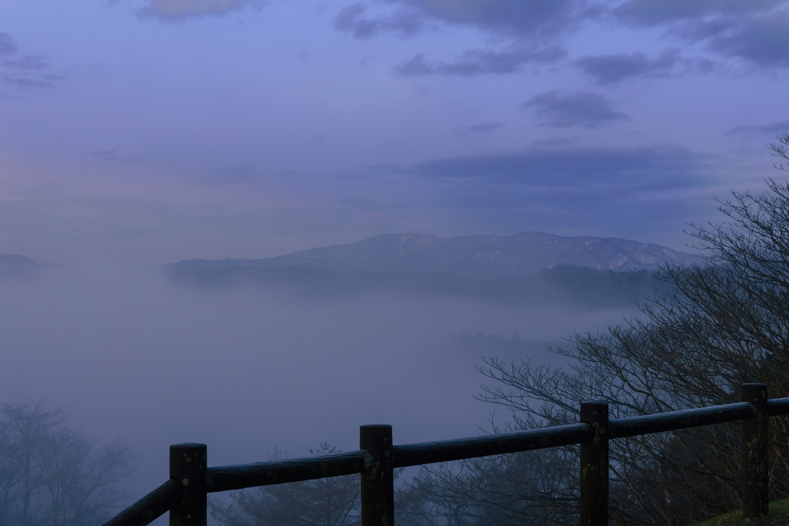 Foggy landscape with silhouettes of mountains and trees at dusk