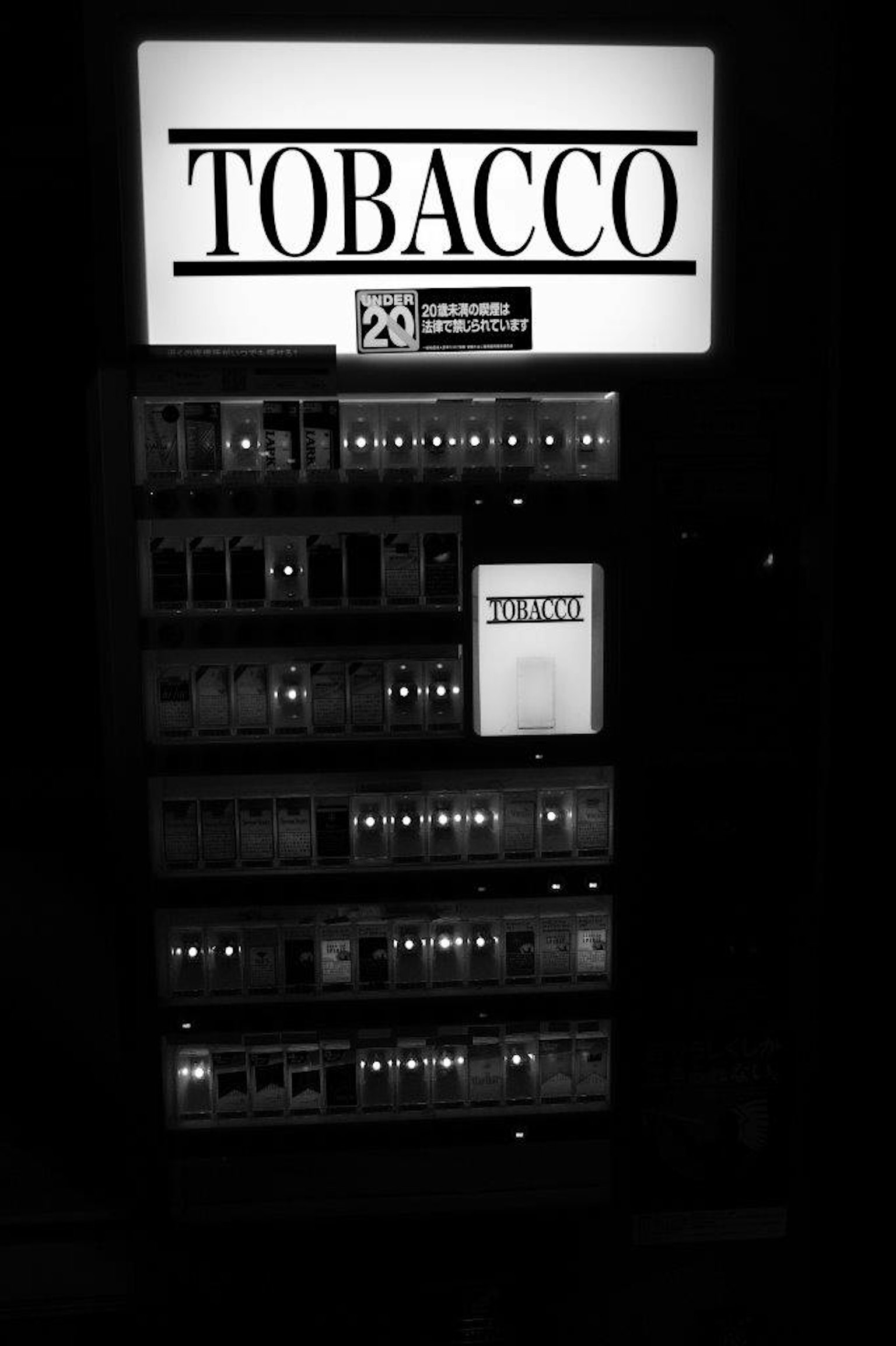 Immagine in bianco e nero di un distributore automatico di tabacco con la scritta Tabacco e diverse opzioni di prodotto