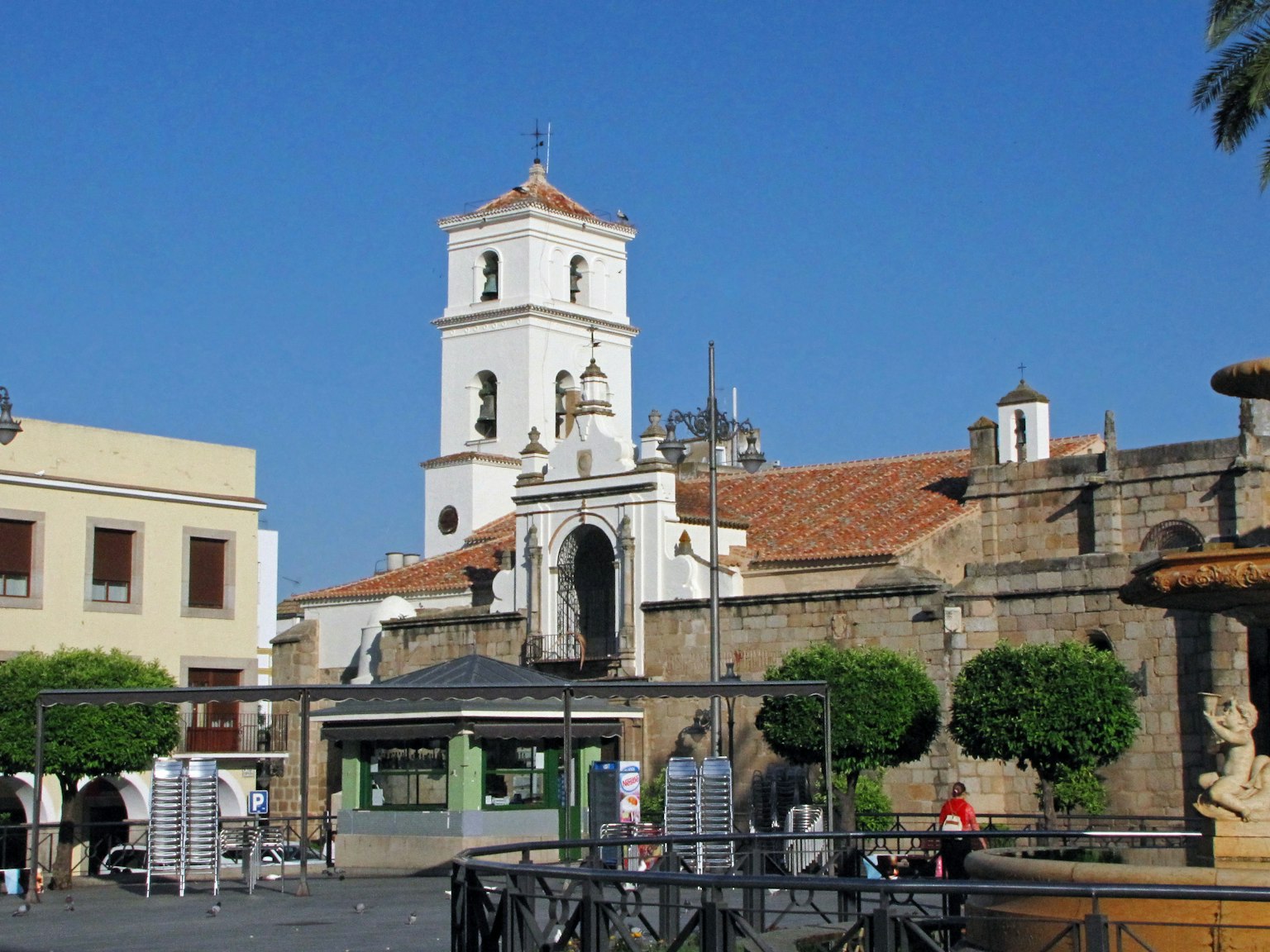 Torre di una chiesa storica in una piazza vivace con edifici circostanti