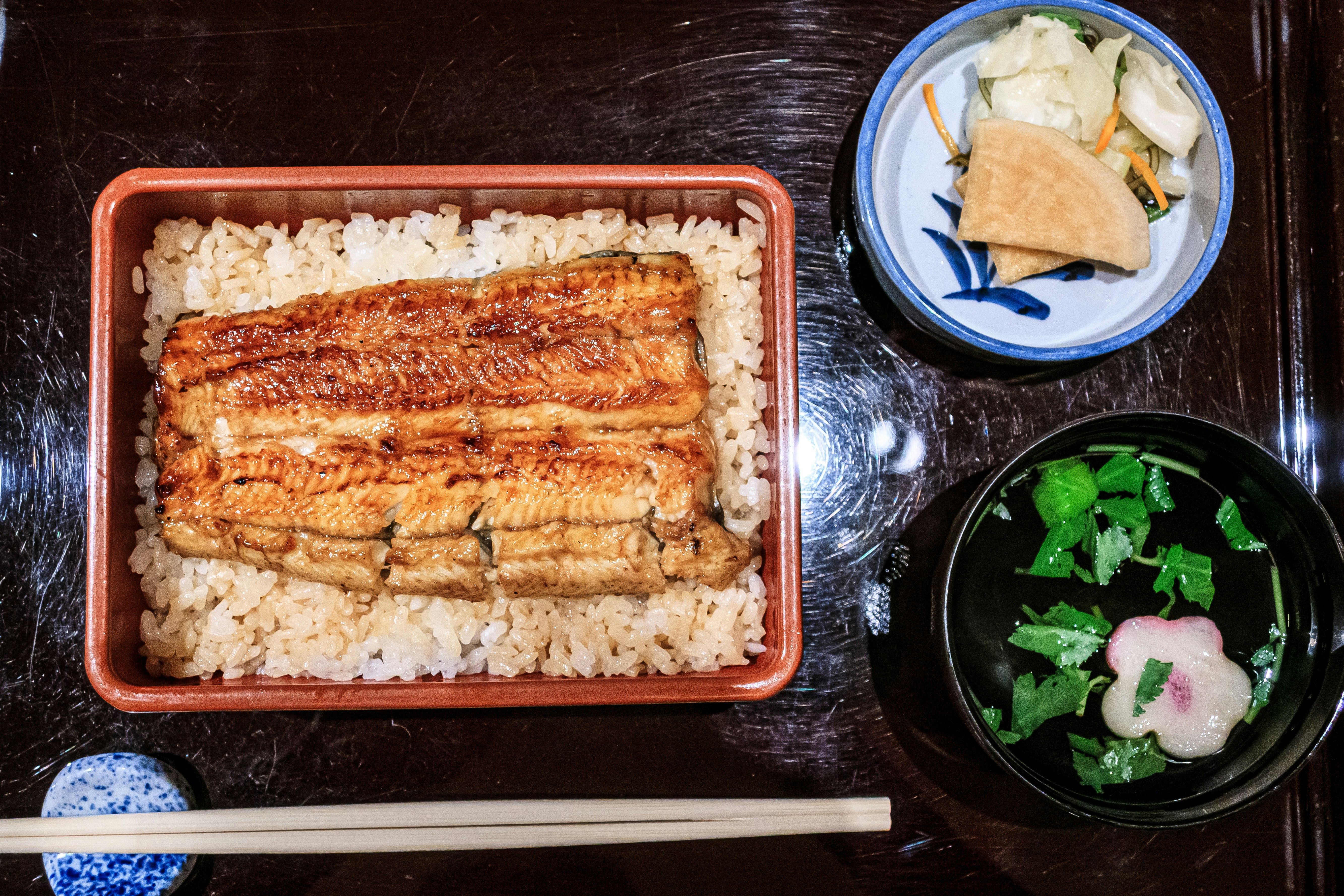 長方形のうな重と小鉢の漬物・味噌汁が並ぶ和食の食卓