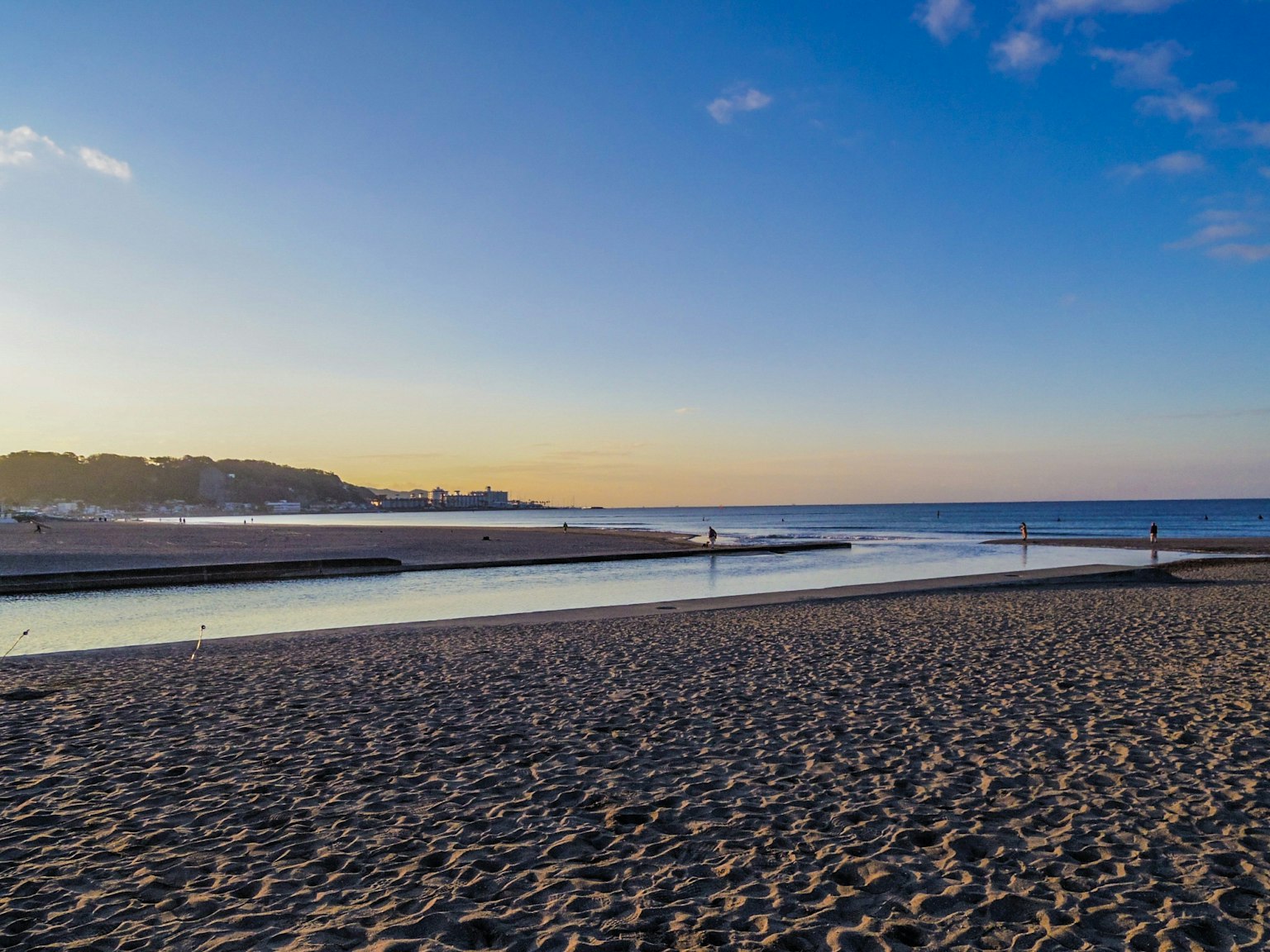 ทิวทัศน์ชายหาดยามพระอาทิตย์ตกน้ำสงบและผู้คนเดิน