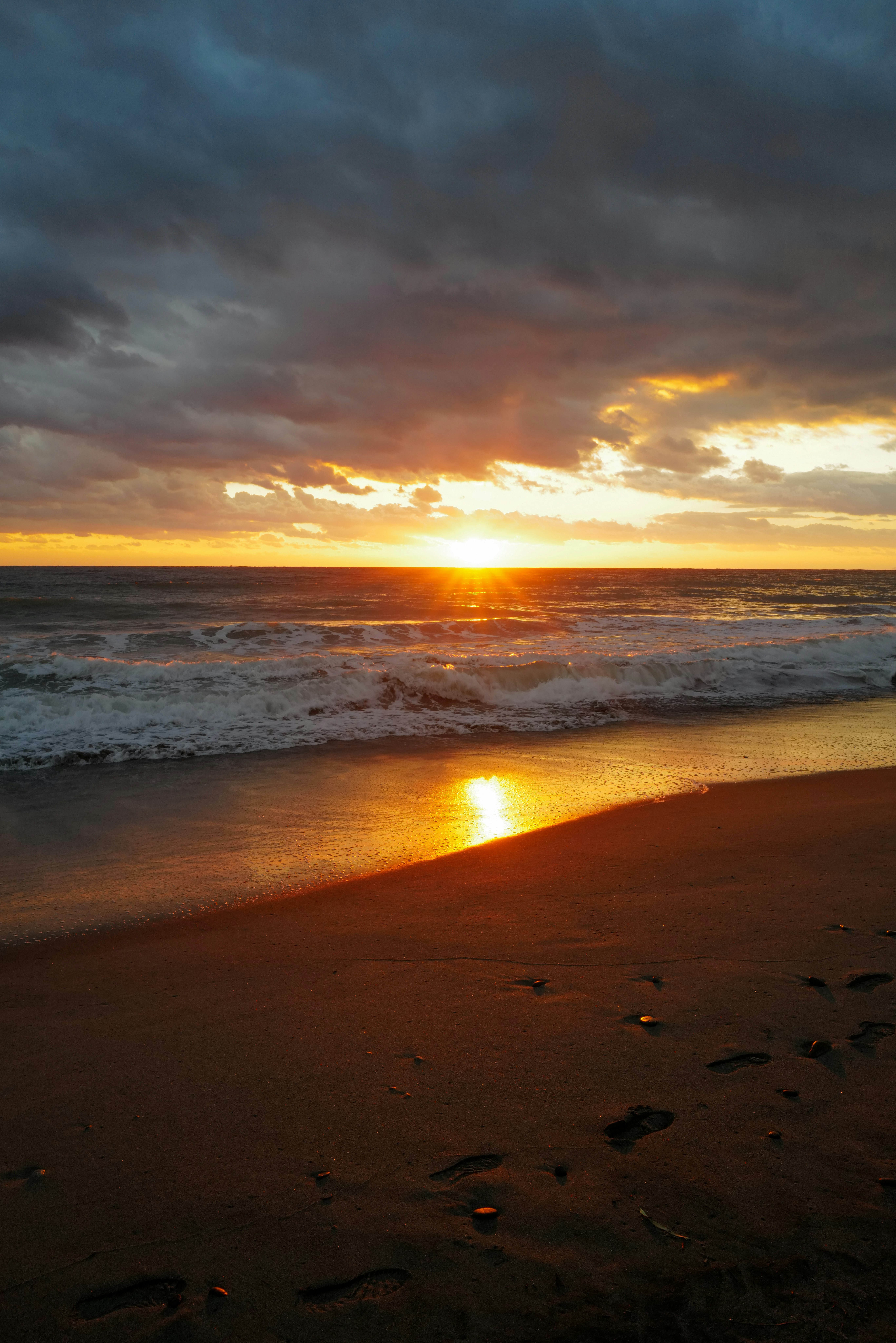 pantai saat matahari terbenam dengan ombak dan cahaya keemasan
