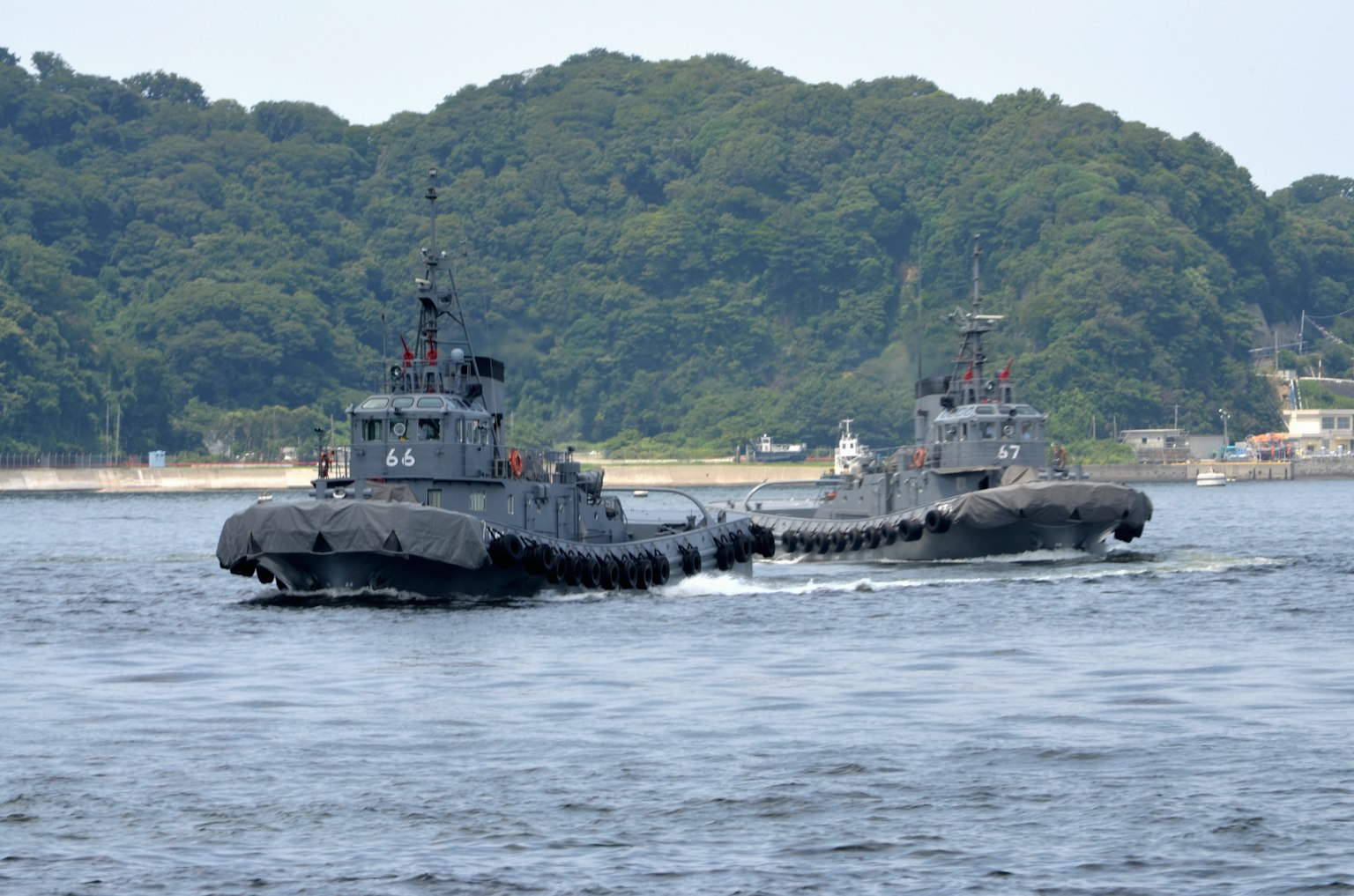 兩艘海軍船隻在海上航行，背景是綠色的山丘