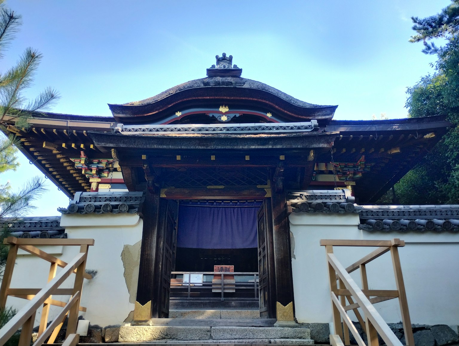 Eingang eines traditionellen japanischen Tempels mit Holzstruktur blauer Vorhang Steinstufen und umgebender Natur