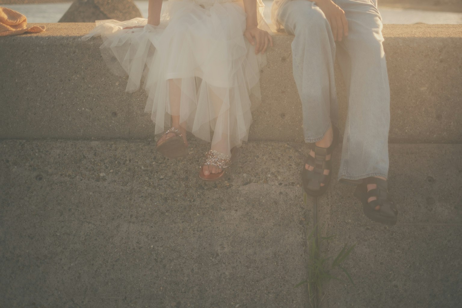 白いドレスを着た女性とカジュアルな服装の男性がコンクリートの壁に座っている