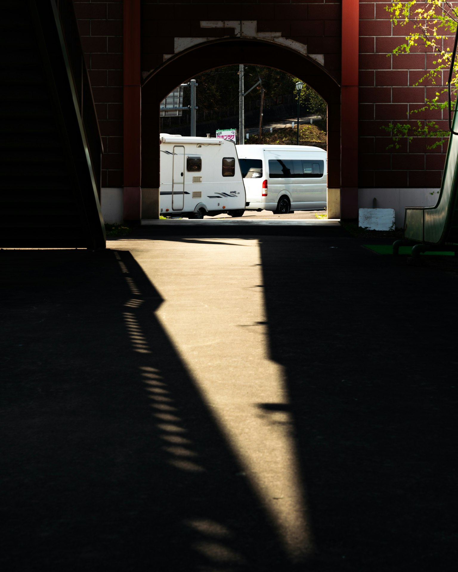 Blick durch ein Torbogen mit einem weißen Bus und Schatten auf dem Gehweg