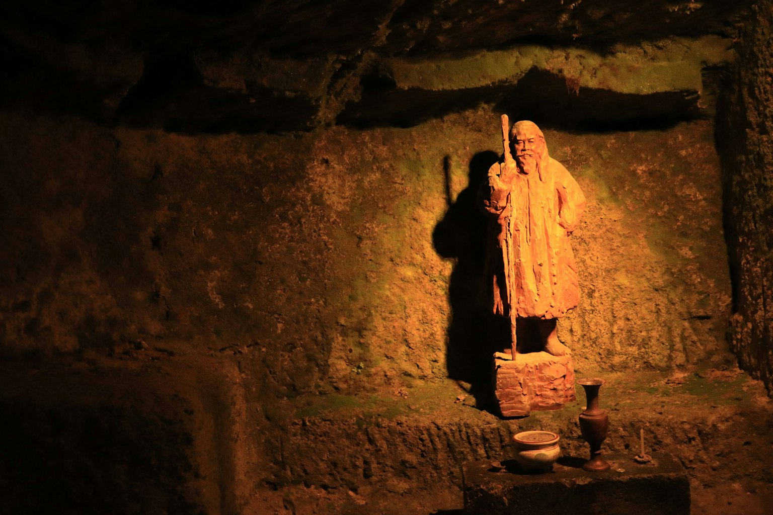 Statue ancienne illuminée dans une grotte sombre avec une ombre projetée sur le mur