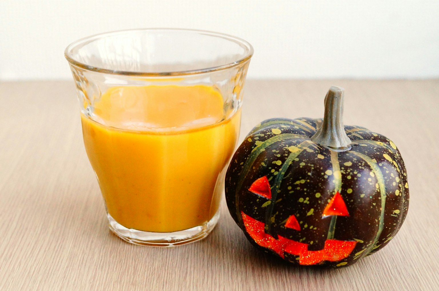 Un vaso de jugo de naranja al lado de una calabaza decorada con una cara de jack-o'-lantern