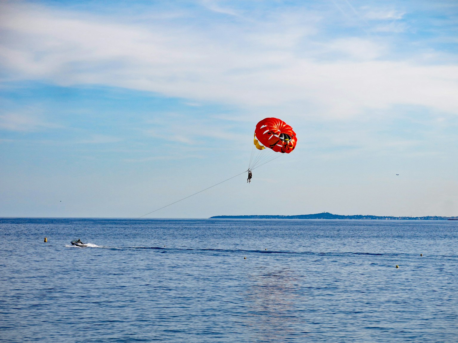 Un paracaídas rojo volando sobre el océano azul con una persona haciendo parasailing