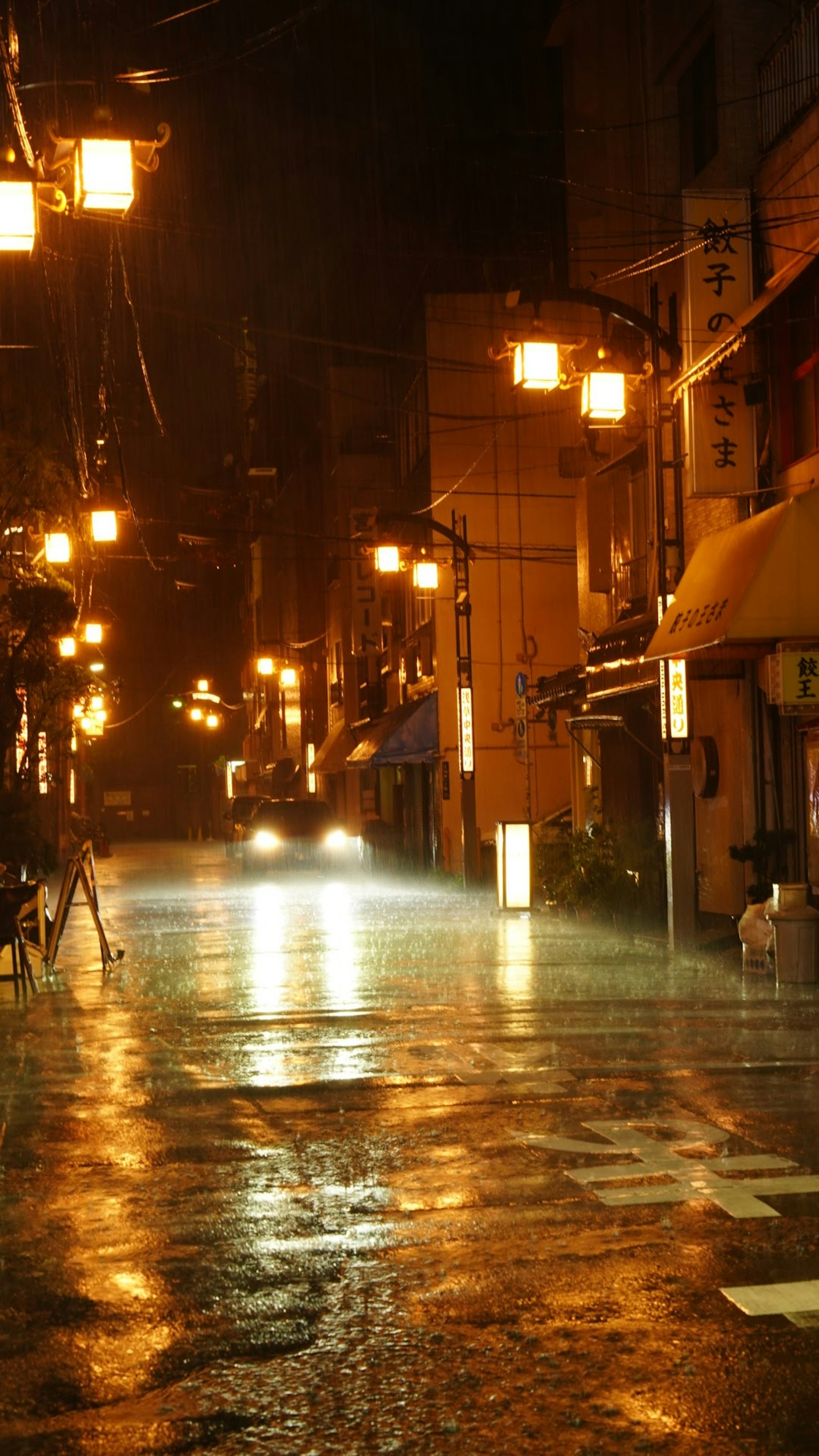 A wet street at night illuminated by warm street lamps