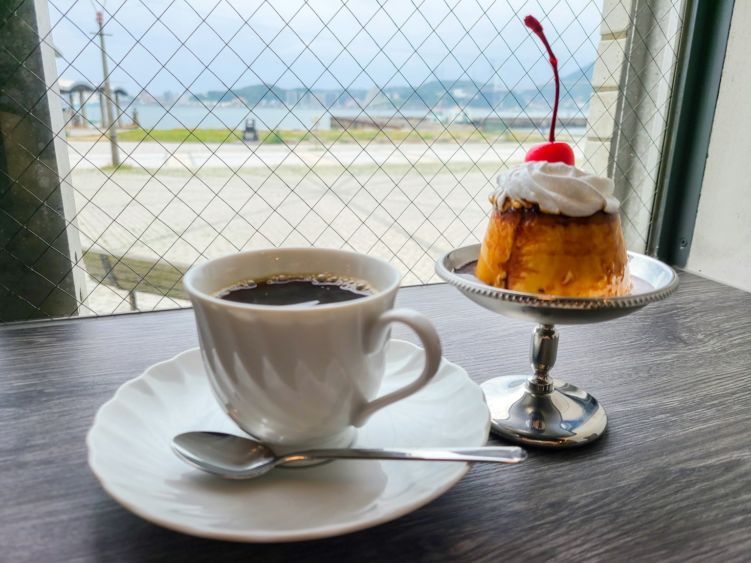 Tasse de café et dessert garni d'une cerise sur une table de café avec vue sur la mer