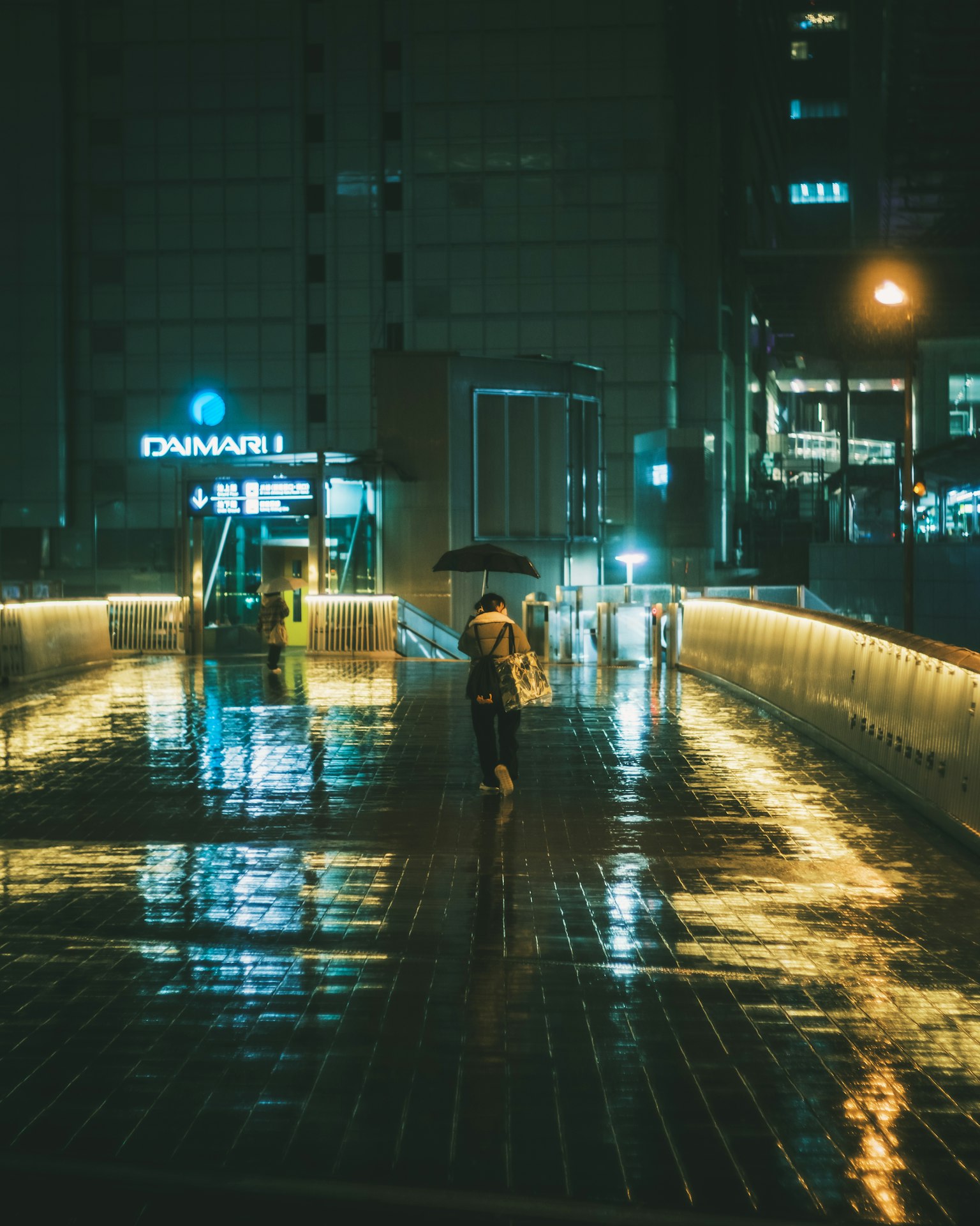 คนเดินถือร่มในคืนฝนตกสะท้อนแสงบนทางเท้า