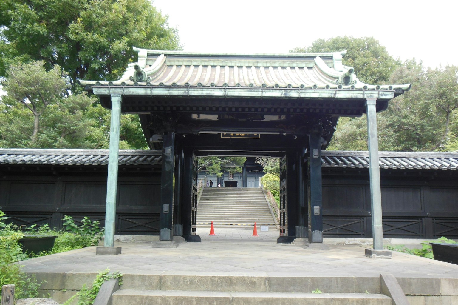 Traditionelles japanisches Tor umgeben von schwarzen Mauern und grünen Bäumen