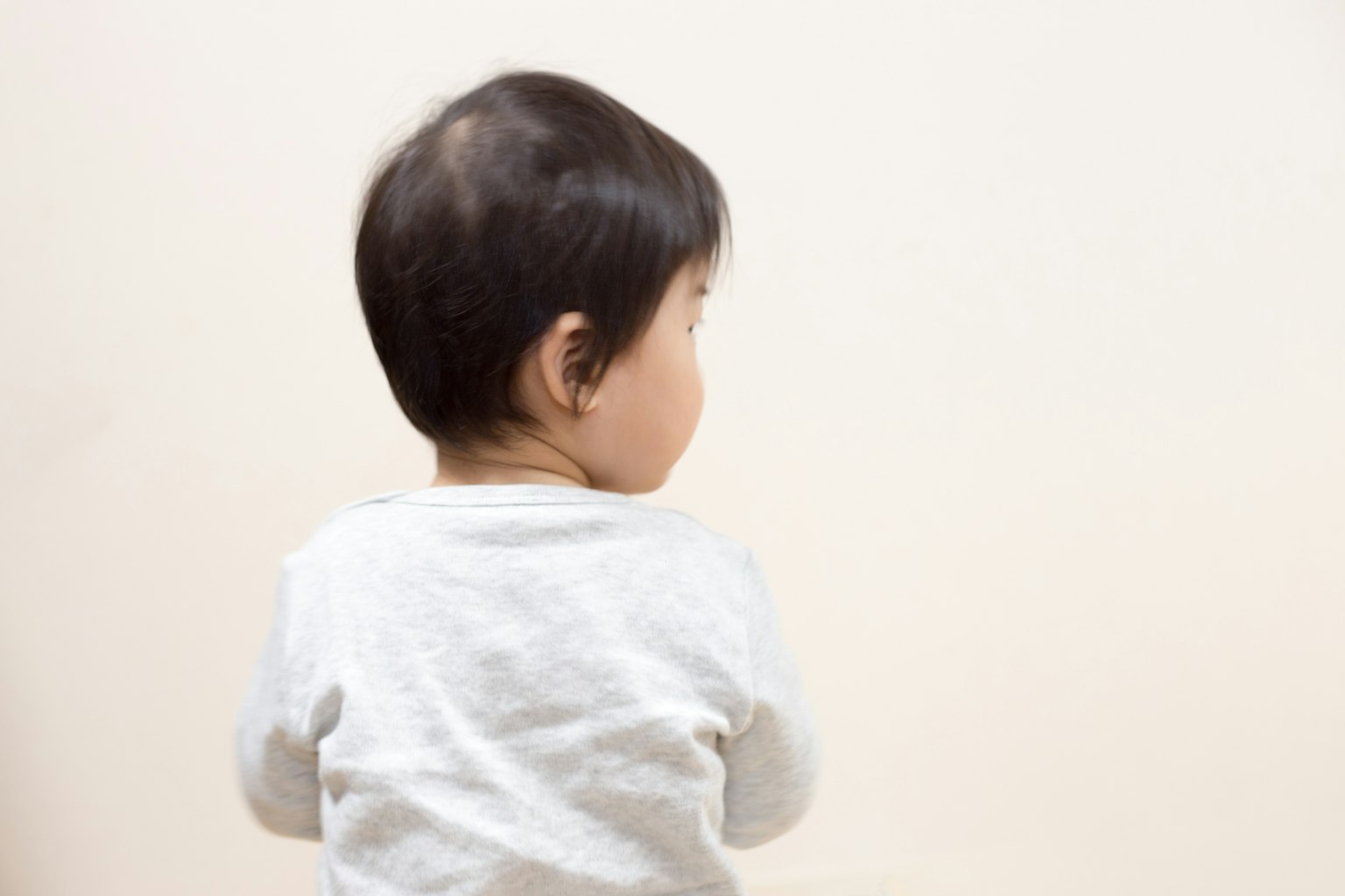 Un bambino visto di spalle con capelli scuri corti su uno sfondo chiaro