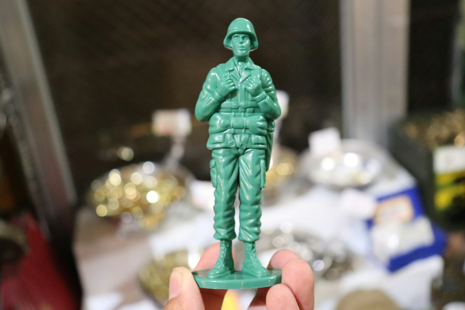 Main tenant une figurine de soldat verte divers objets métalliques en arrière-plan