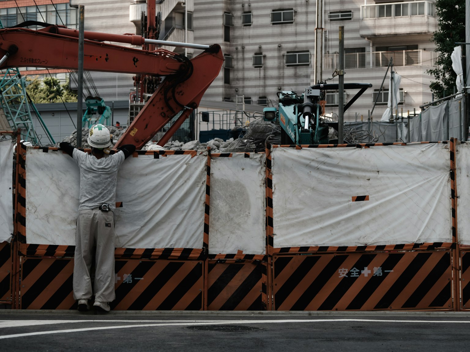 Arbeiter auf einer Baustelle, der sich an einer orange-schwarzen Barrikade lehnt