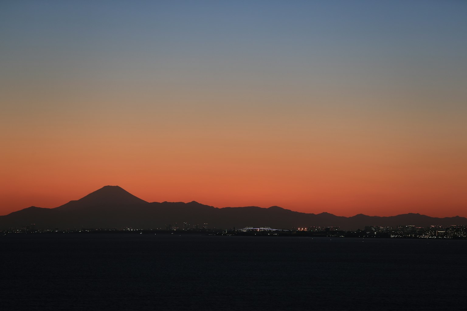 Silueta de montañas al atardecer con luces de la ciudad