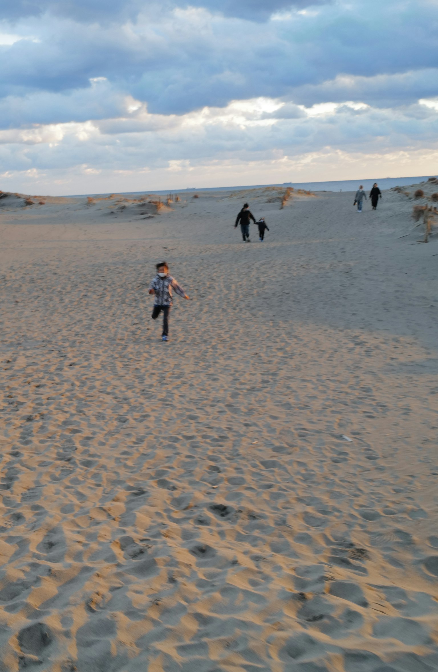 Un niño corriendo en dunas de arena con personas al fondo