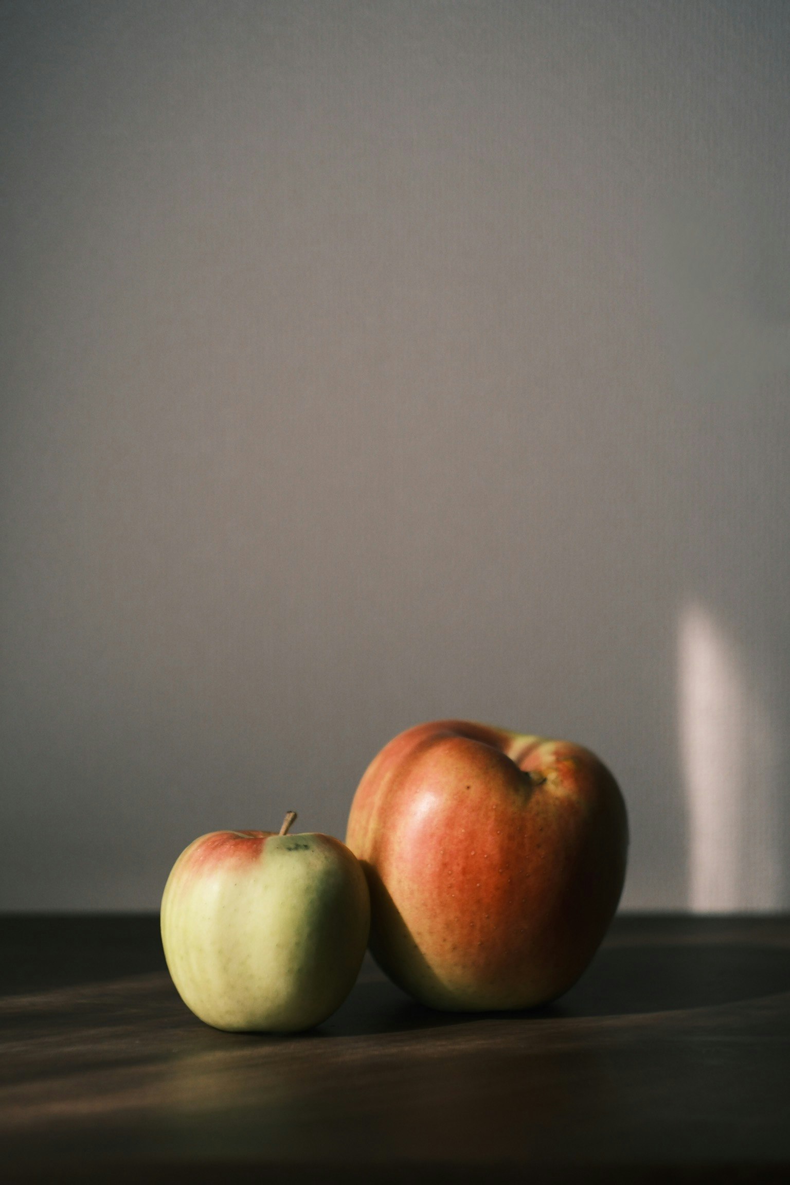 赤と緑のリンゴが木のテーブルの上に置かれているシンプルな構図