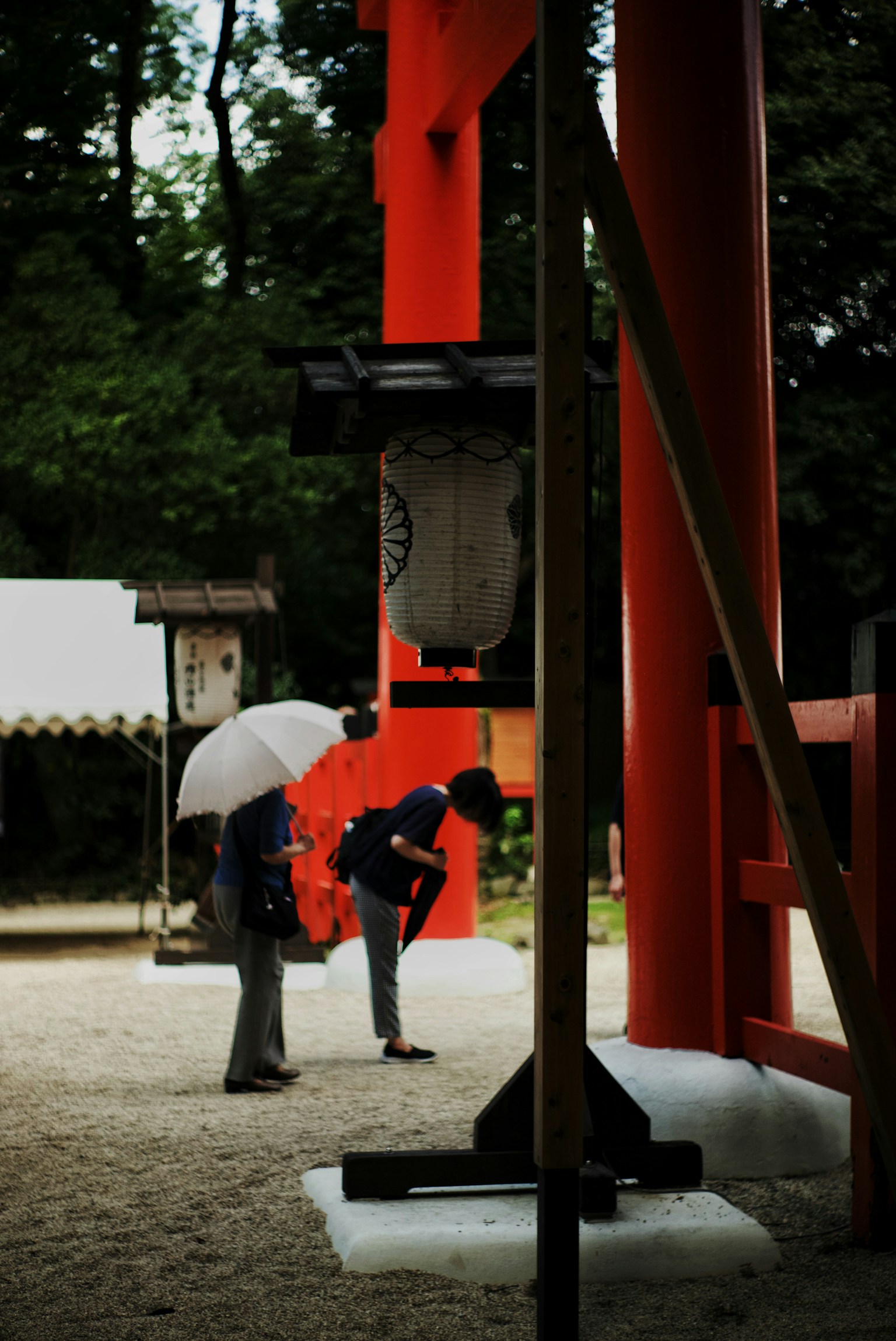 赤い鳥居の下でお辞儀をする人々と傘