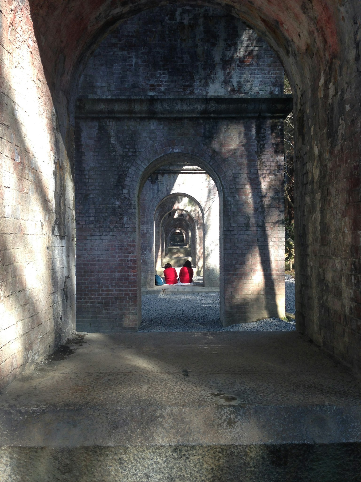 Due persone in abiti rossi che camminano attraverso un vecchio tunnel ad arco