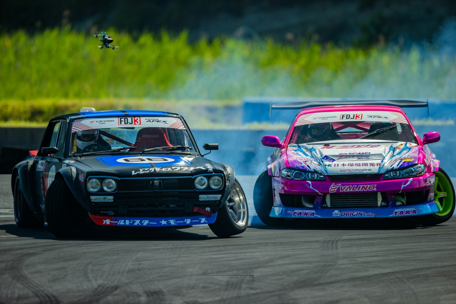 Deux voitures de drift en compétition sur une piste avec des designs colorés et de la fumée
