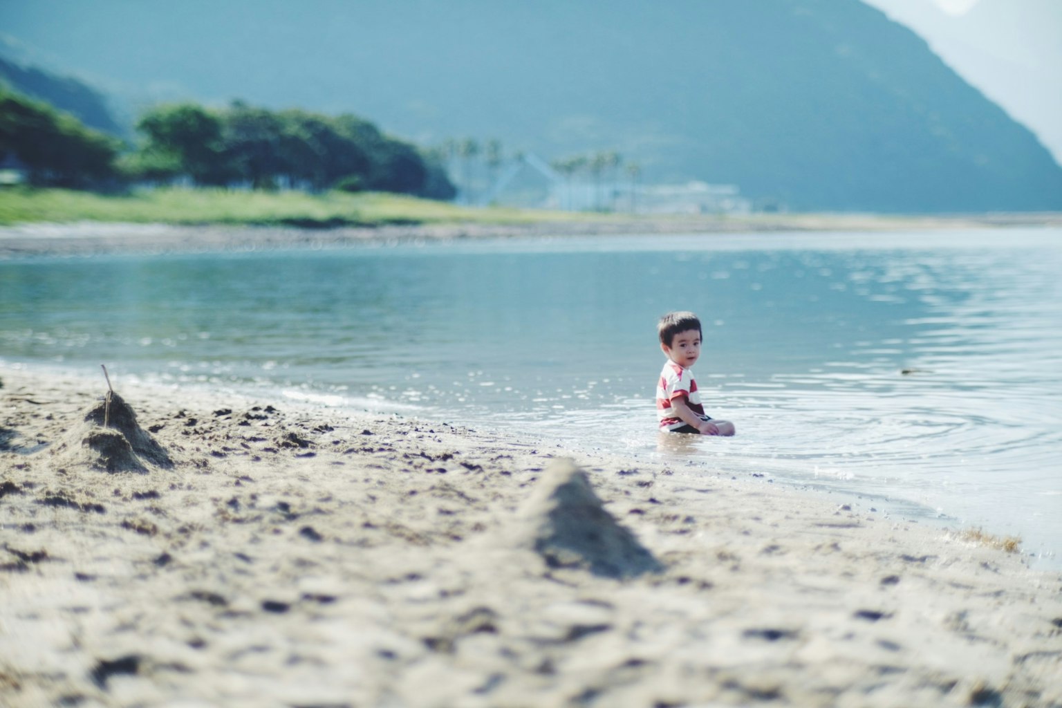 Enfant jouant sur la plage avec des montagnes et de l'eau bleue en arrière-plan