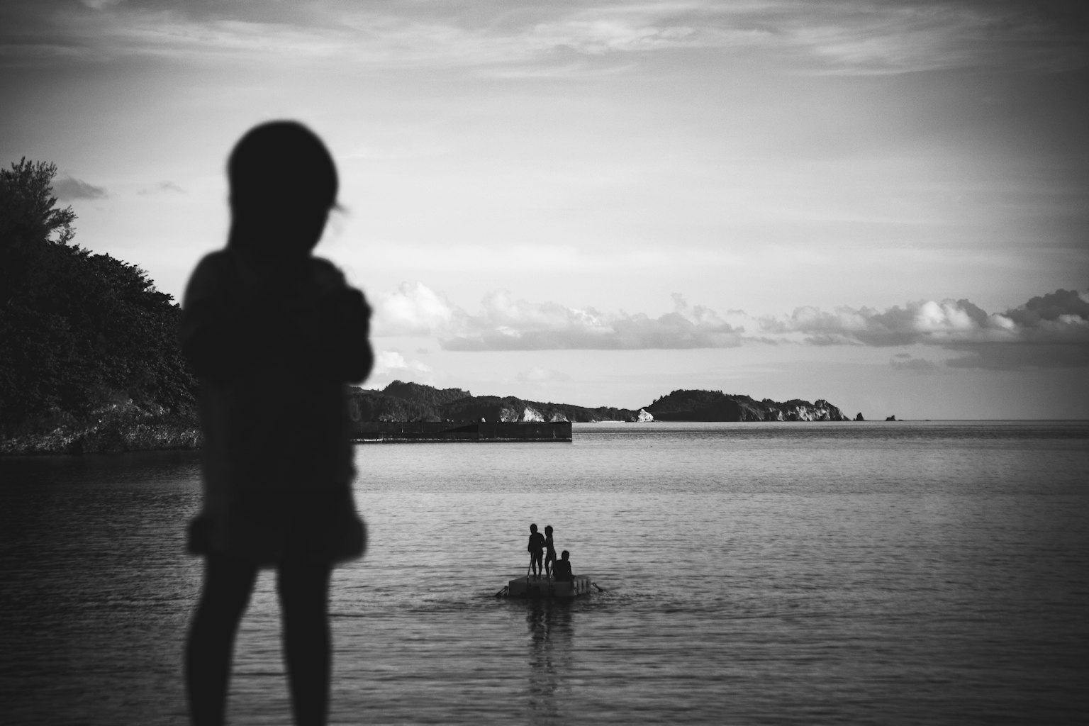 Siluet seorang anak yang melihat laut dengan perahu kecil di latar belakang