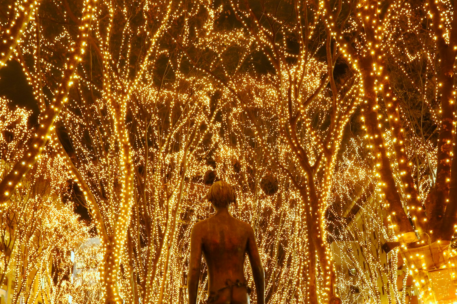 Statue standing among trees adorned with warm lights