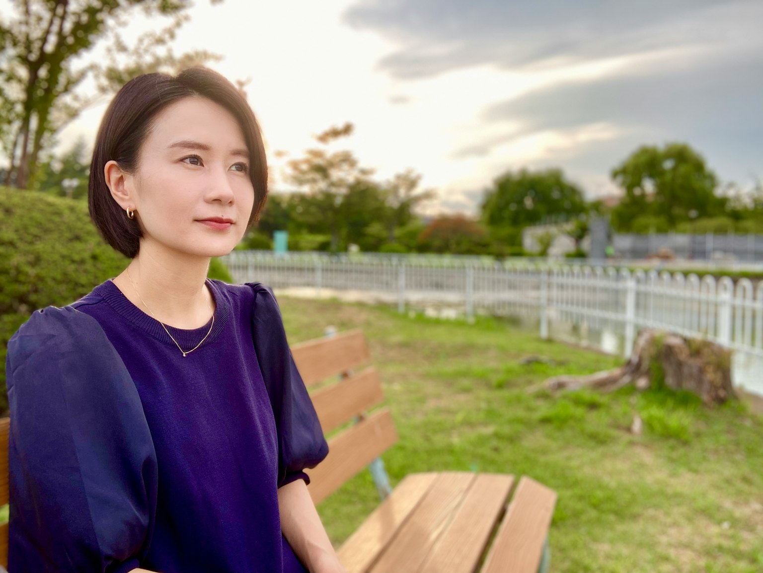 자주색 상의를 입은 여성이 일몰 동안 공원 벤치에 앉아 있다