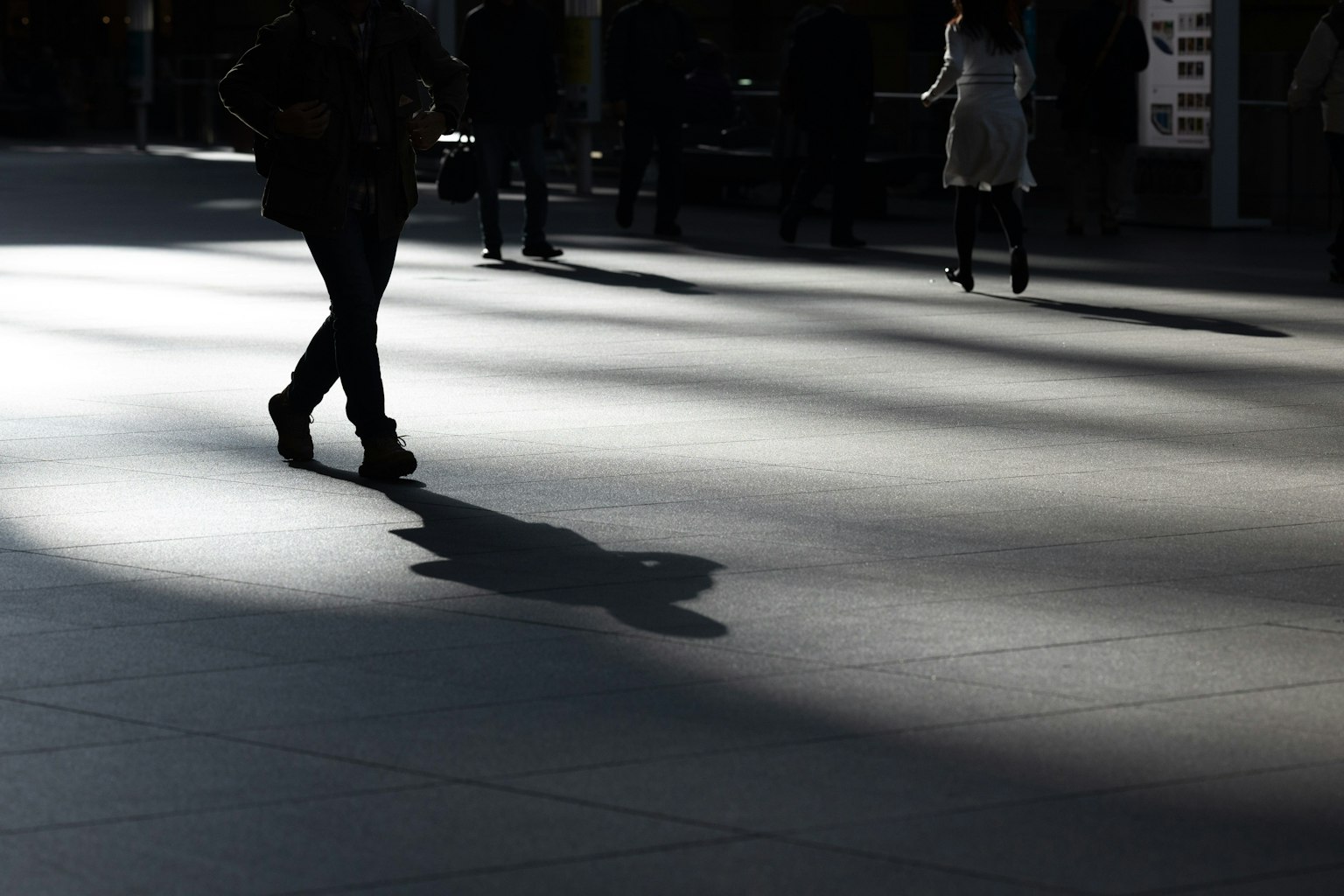 Escena urbana con personas caminando sombras y luz contrastante