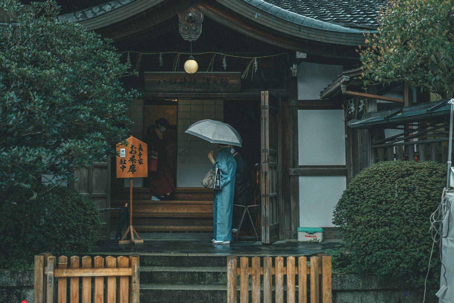 Una persona in kimono blu che tiene un ombrello davanti a un edificio giapponese tradizionale