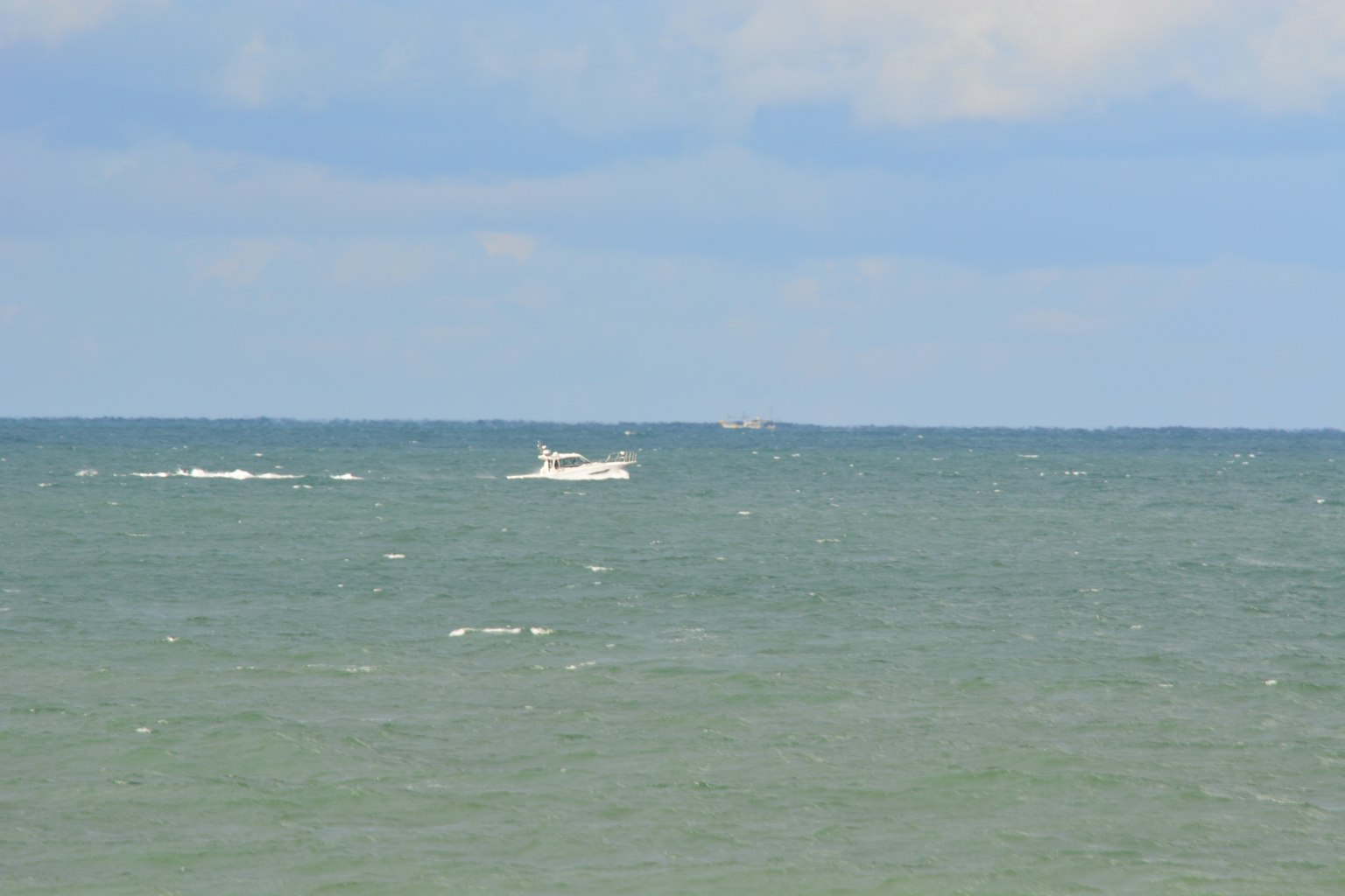一艘小船漂浮在藍色海面上，雲層覆蓋的天空