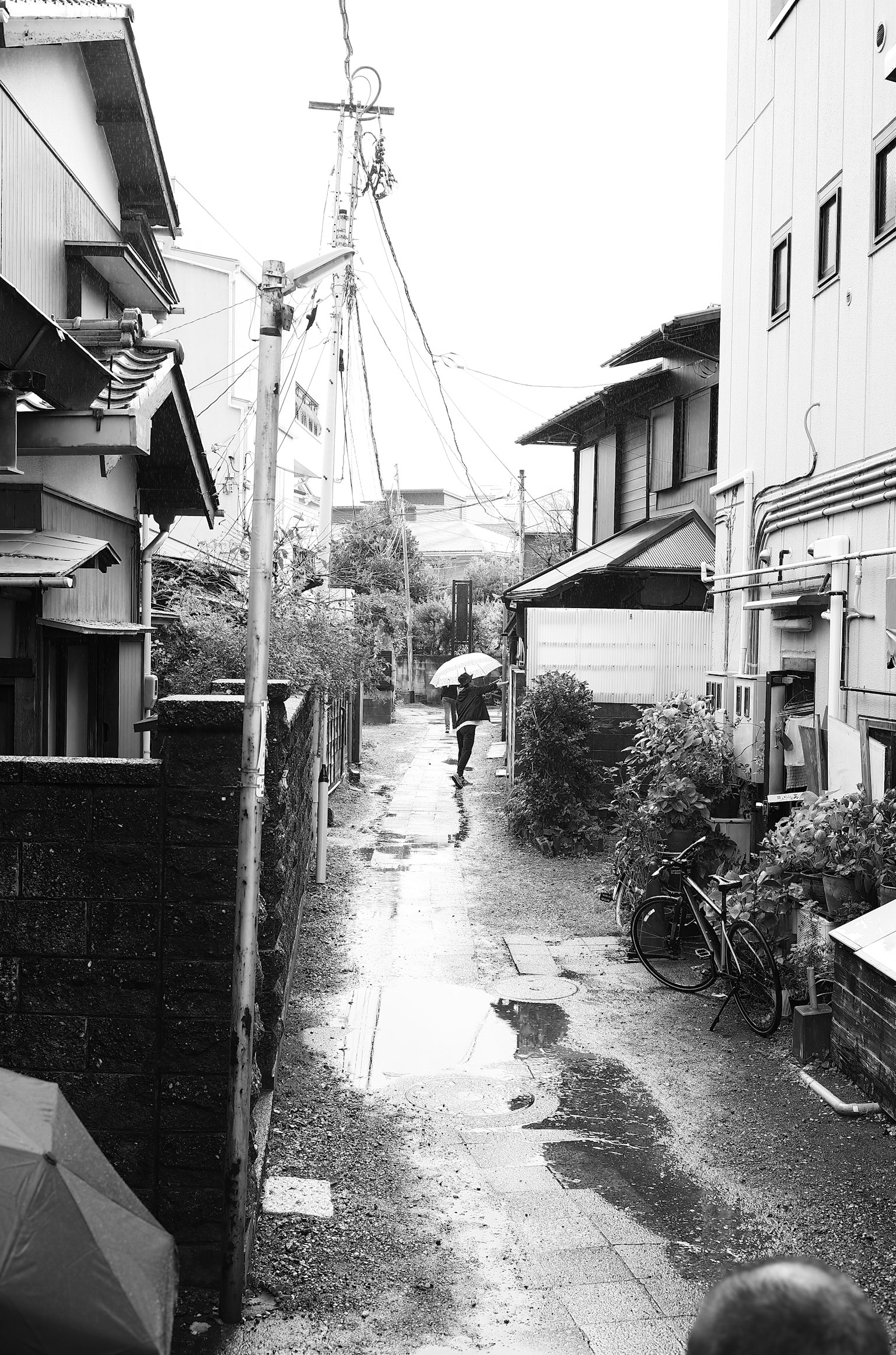 Photo en noir et blanc d'une ruelle étroite par un jour de pluie avec une personne tenant un parapluie