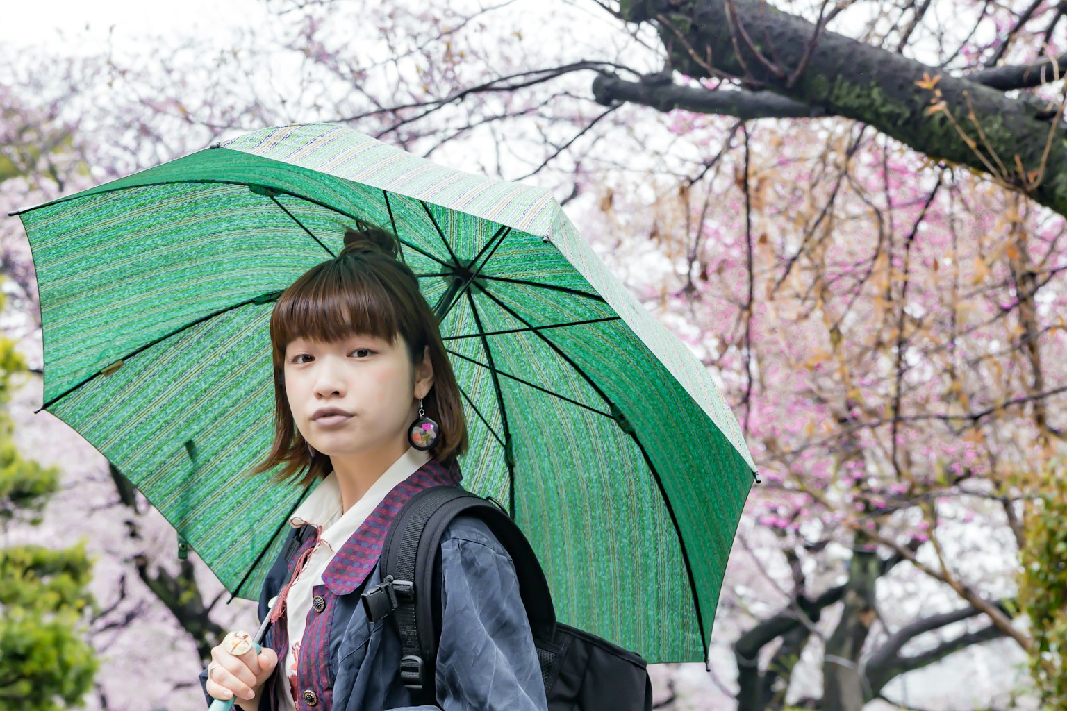 Woman holding a green umbrella among blooming cherry blossoms