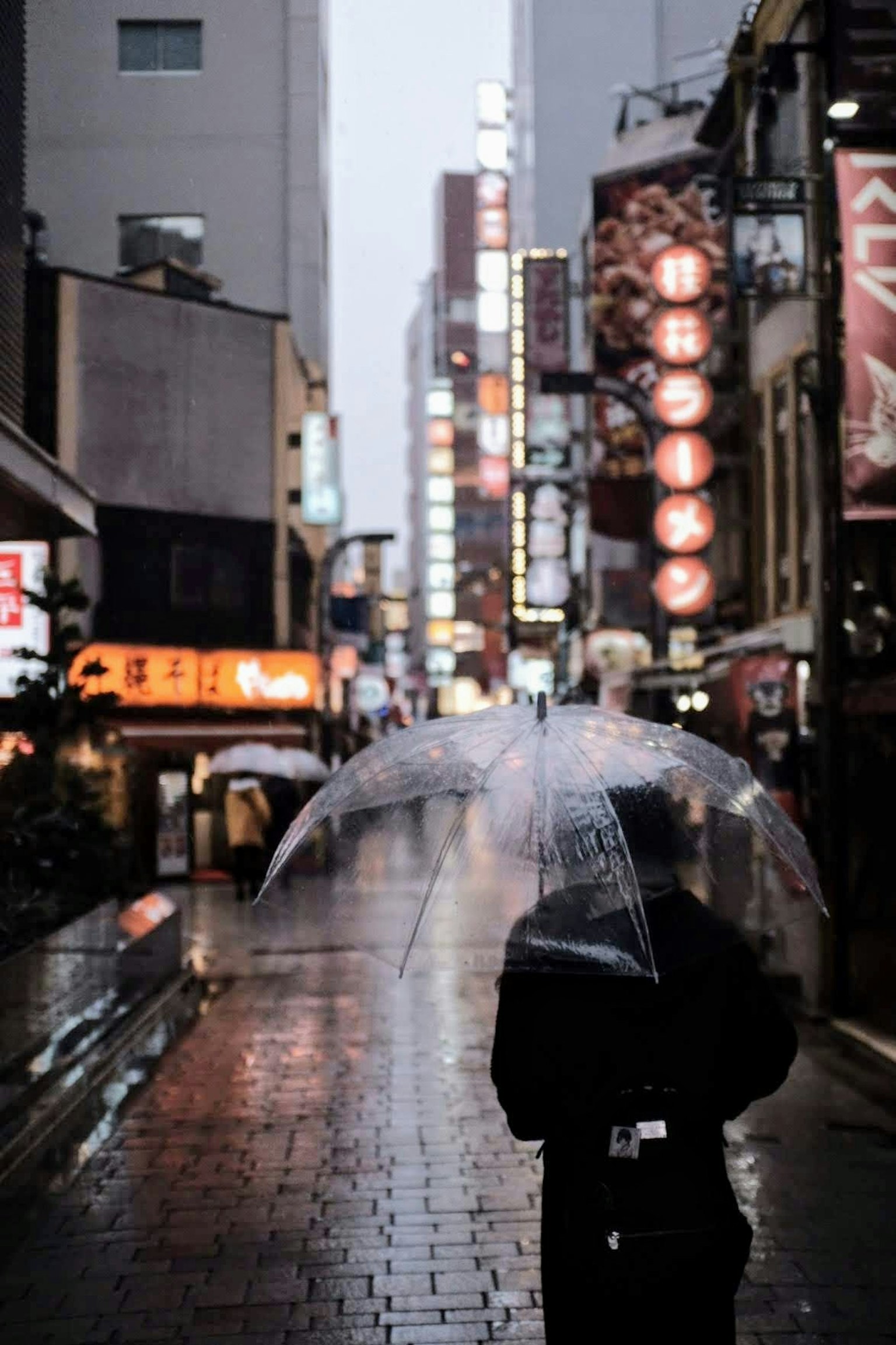 Eine Person mit einem Regenschirm, die durch eine regennasse Stadtstraße geht