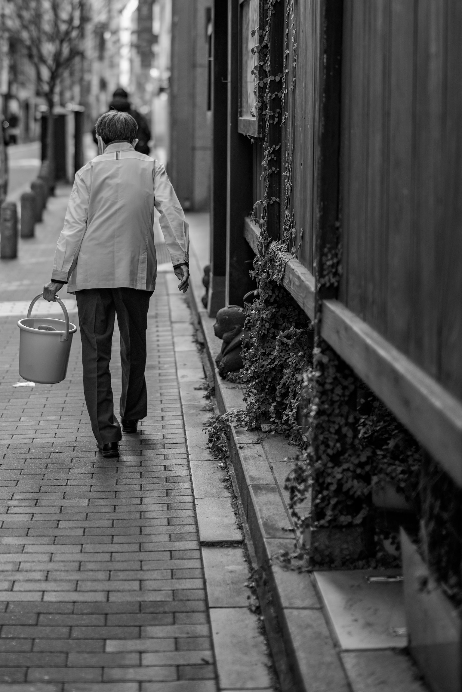 A person walking down a black and white street carrying a bucket