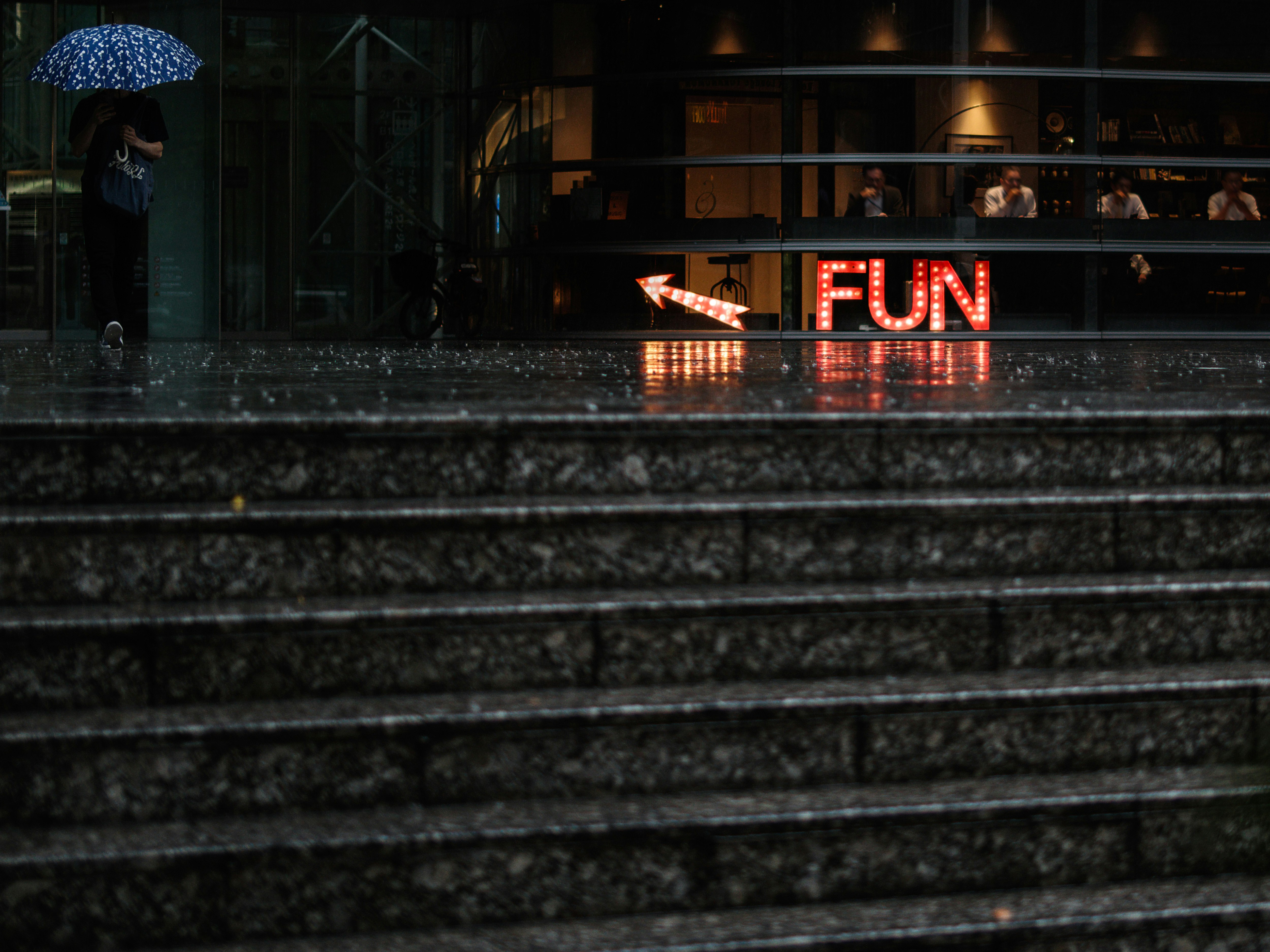 Rainy stone steps with a “FUN” neon sign at a street corner