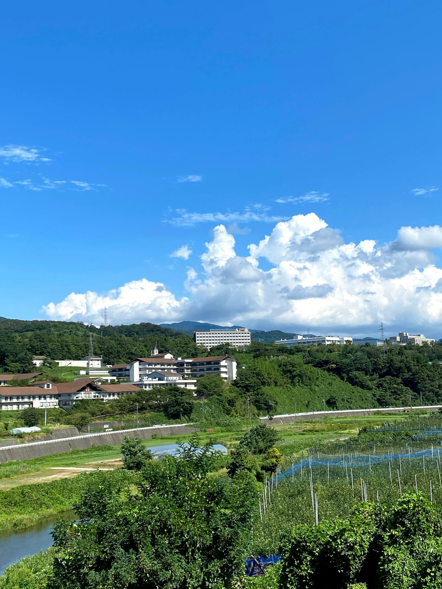 青空と白い雲が広がる風景 緑豊かな丘と川が流れる 住宅と農地が見える