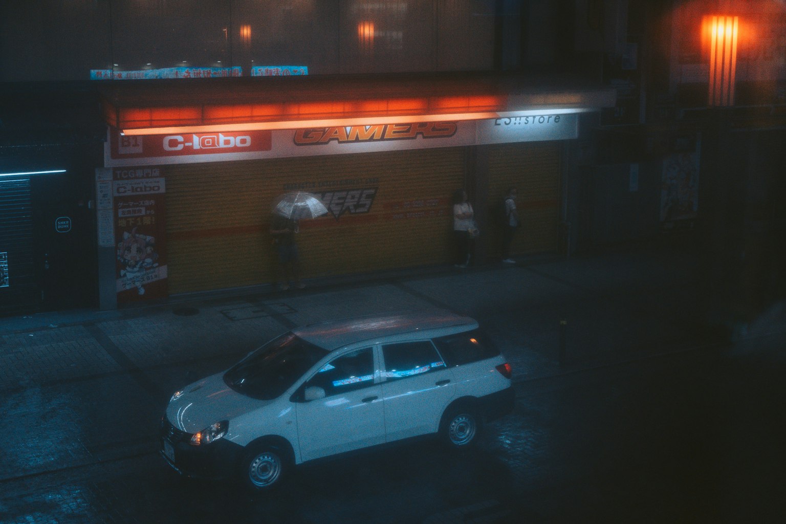 Scène de rue nocturne avec un SUV blanc et l'extérieur d'un café sous la pluie