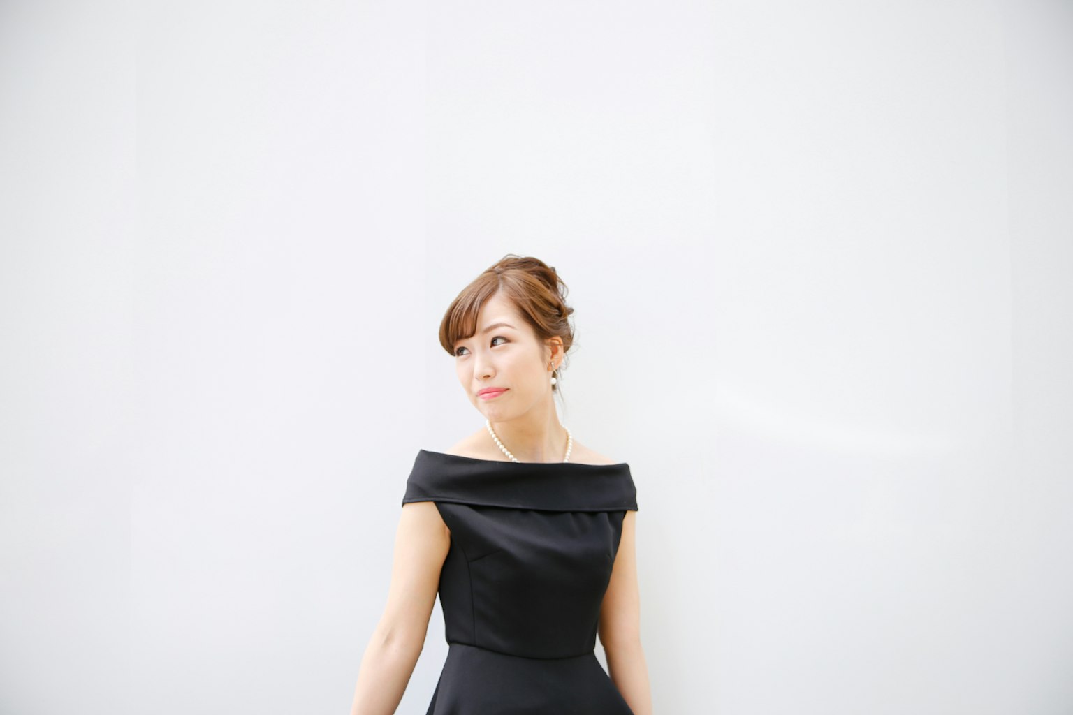 A woman in a black dress stands against a white wall