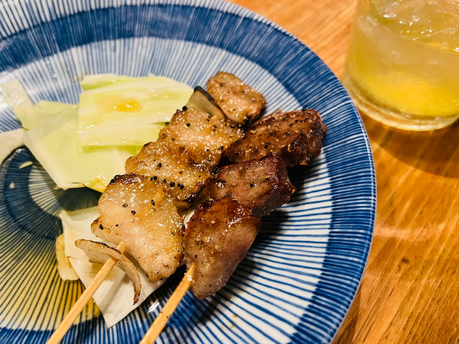 Brochettes de yakitori sur une assiette bleue avec du chou et une boisson