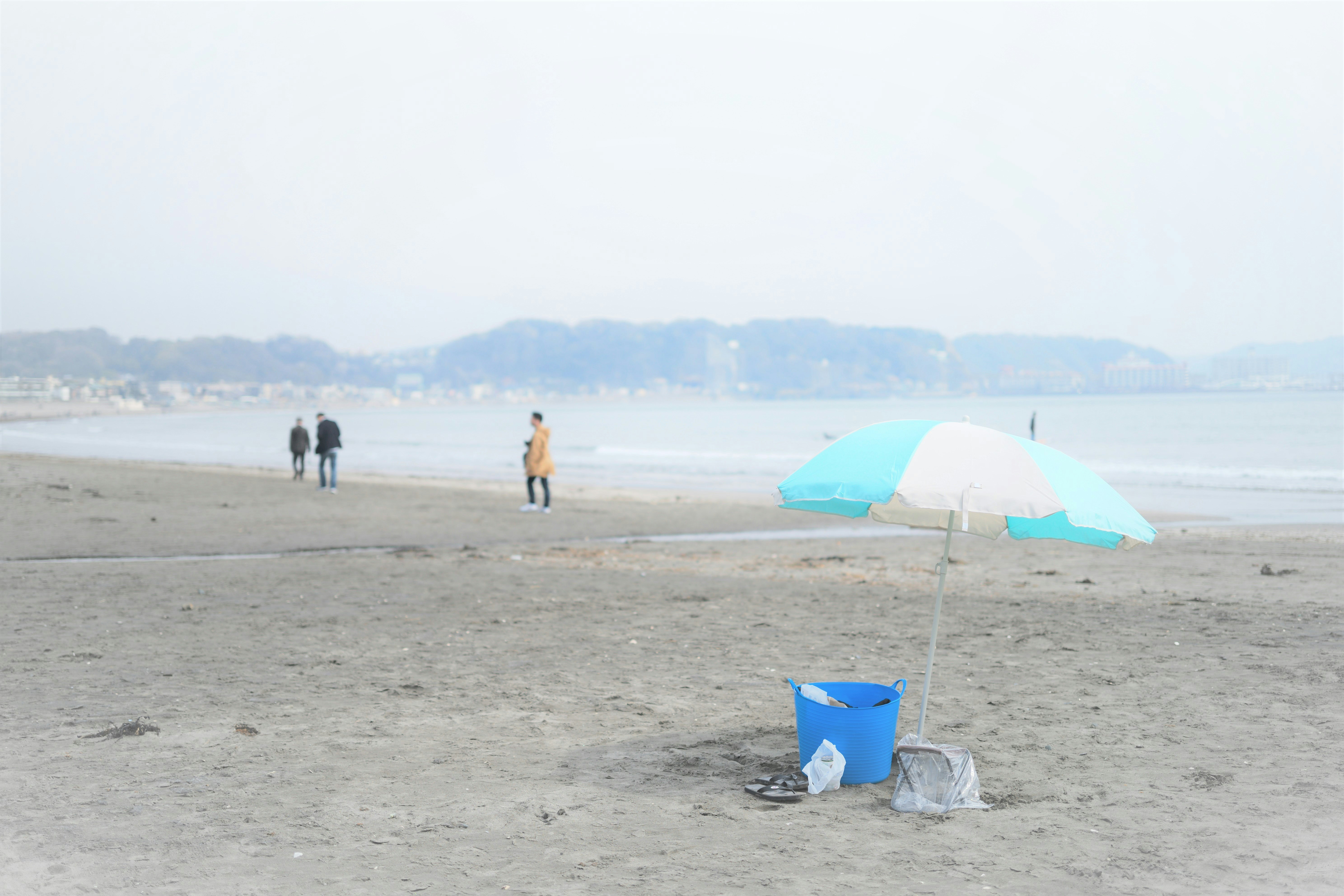 沙灘上擺放的藍色水桶和淺藍色遮陽傘的海邊場景