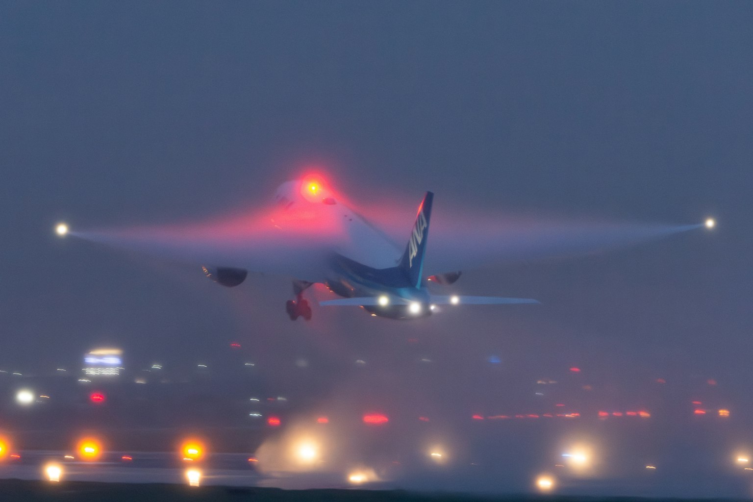 Avion décollant la nuit avec des lumières rouges et un fond brumeux